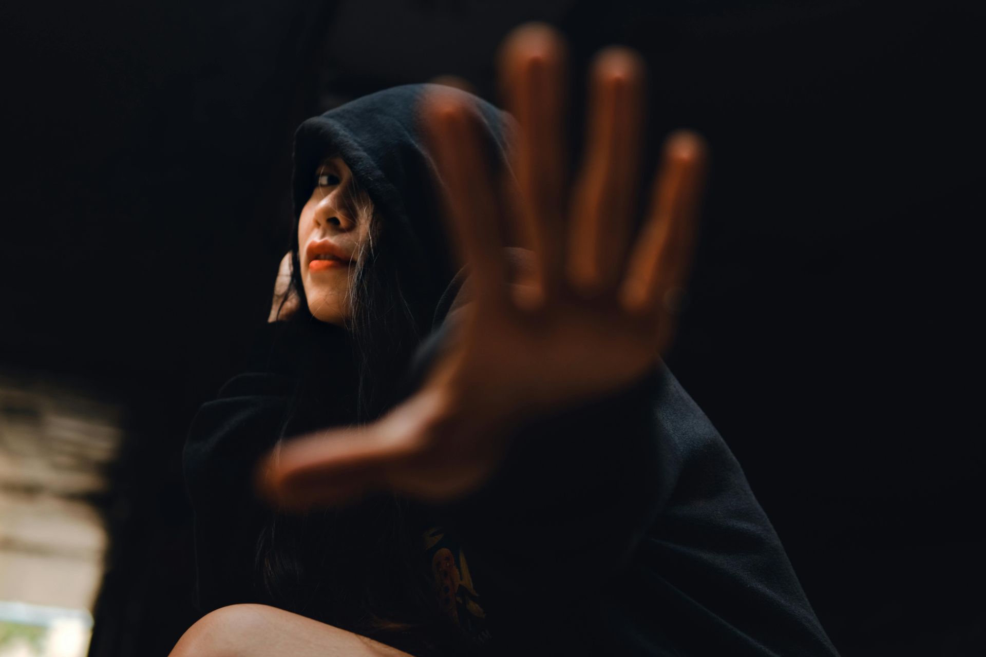 A woman in a black hoodie is making a stop sign with her hand.