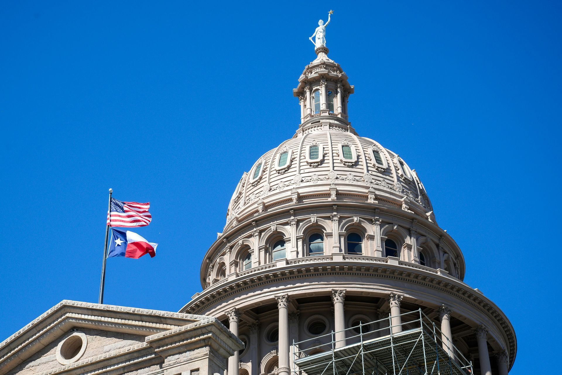Texas State Capitol dome with flags against a clear blue sky