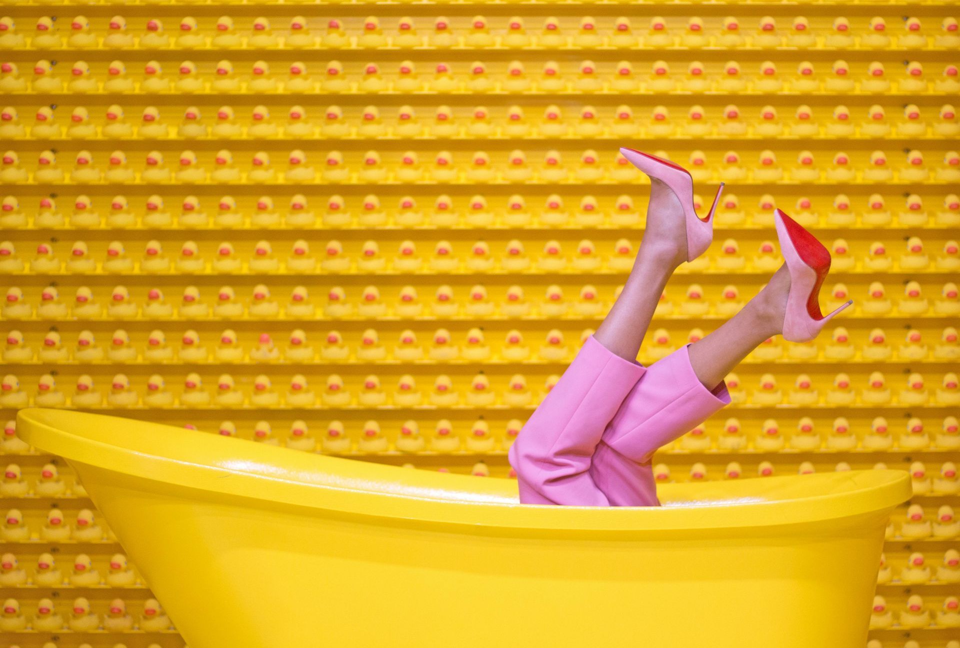 Yellow bathtub with legs in pink pants and shoes up in the air. Yellow wall in background.