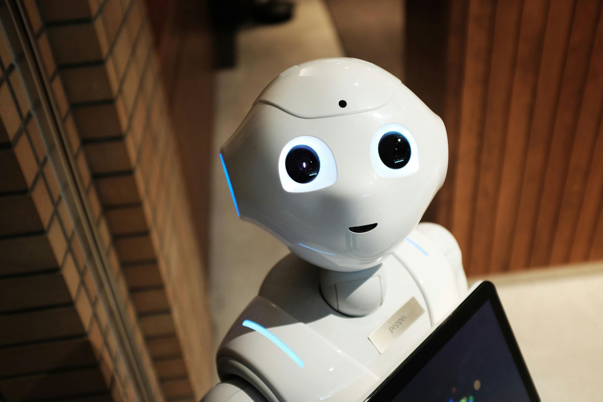 Close-up of a white Pepper humanoid robot with large, glowing eyes, holding a tablet indoors.