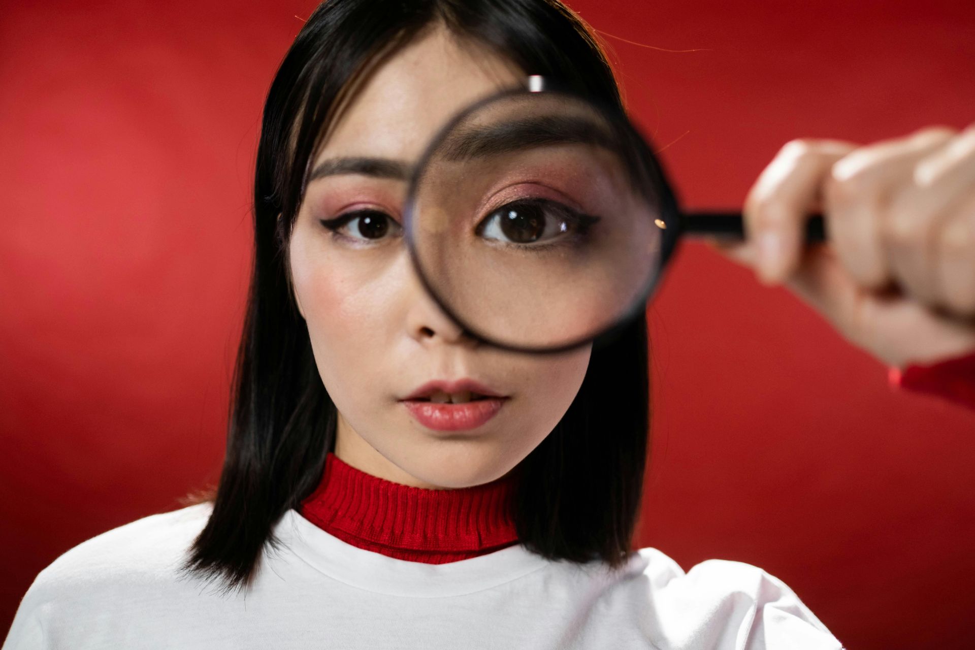 Woman looking intently through magnifying glass; red background.
