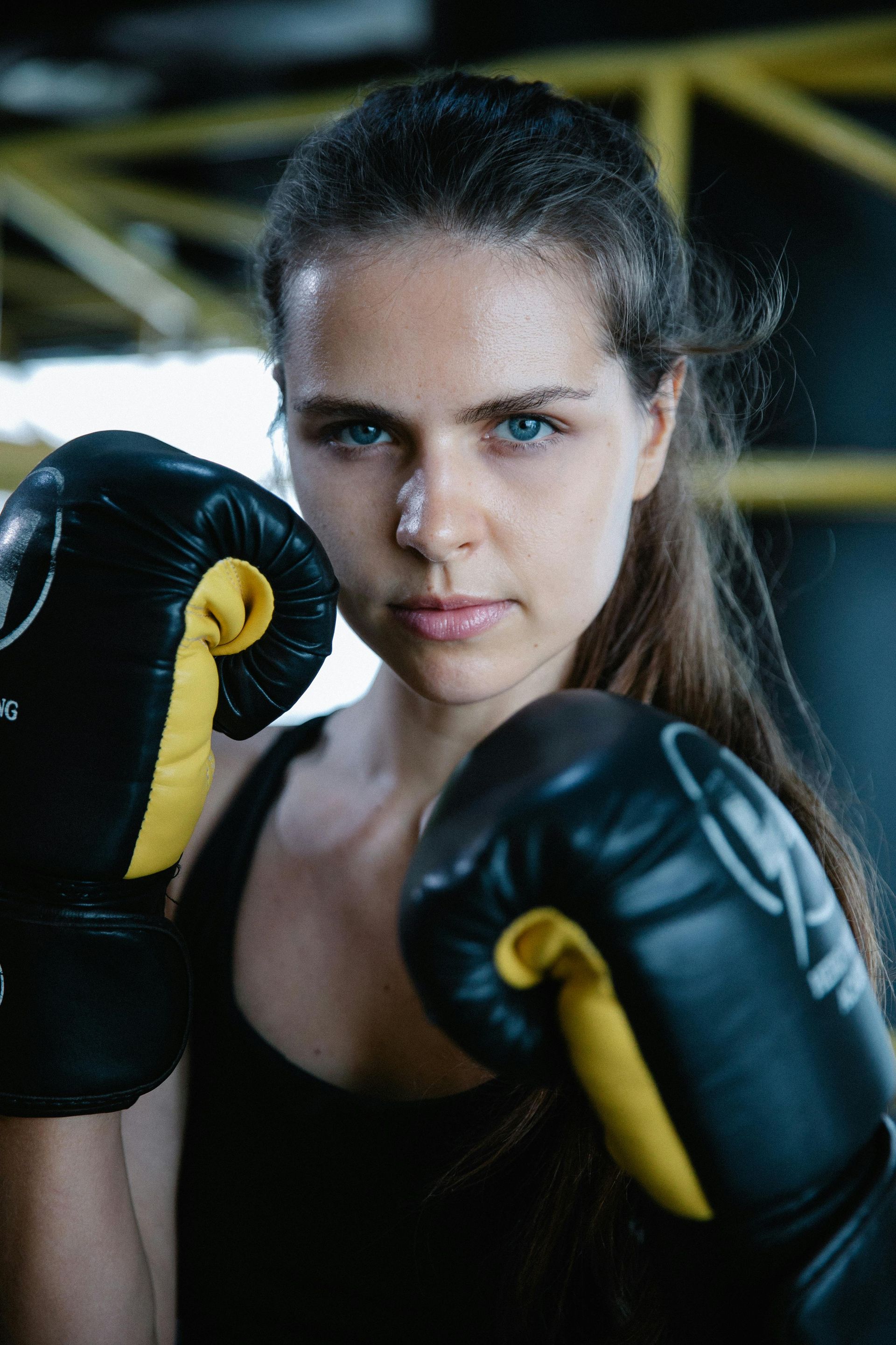 A woman wearing black and yellow boxing gloves is standing in a gym.