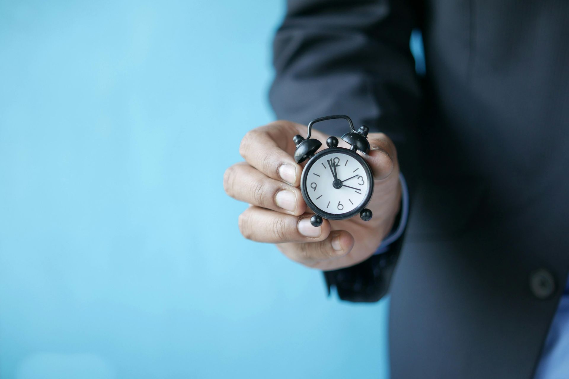 A man in a suit is holding an alarm clock in his hand.