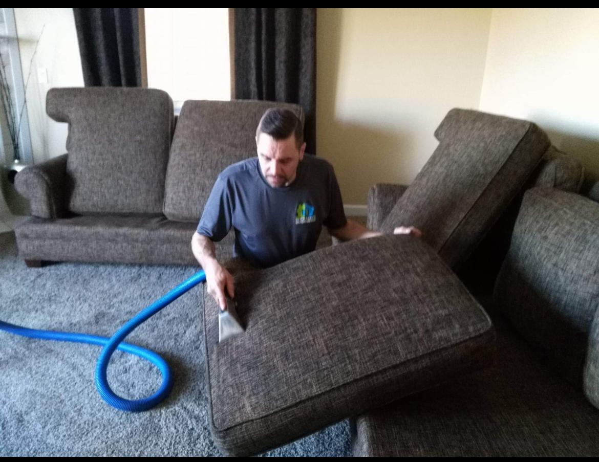 A man is cleaning a couch with a vacuum cleaner