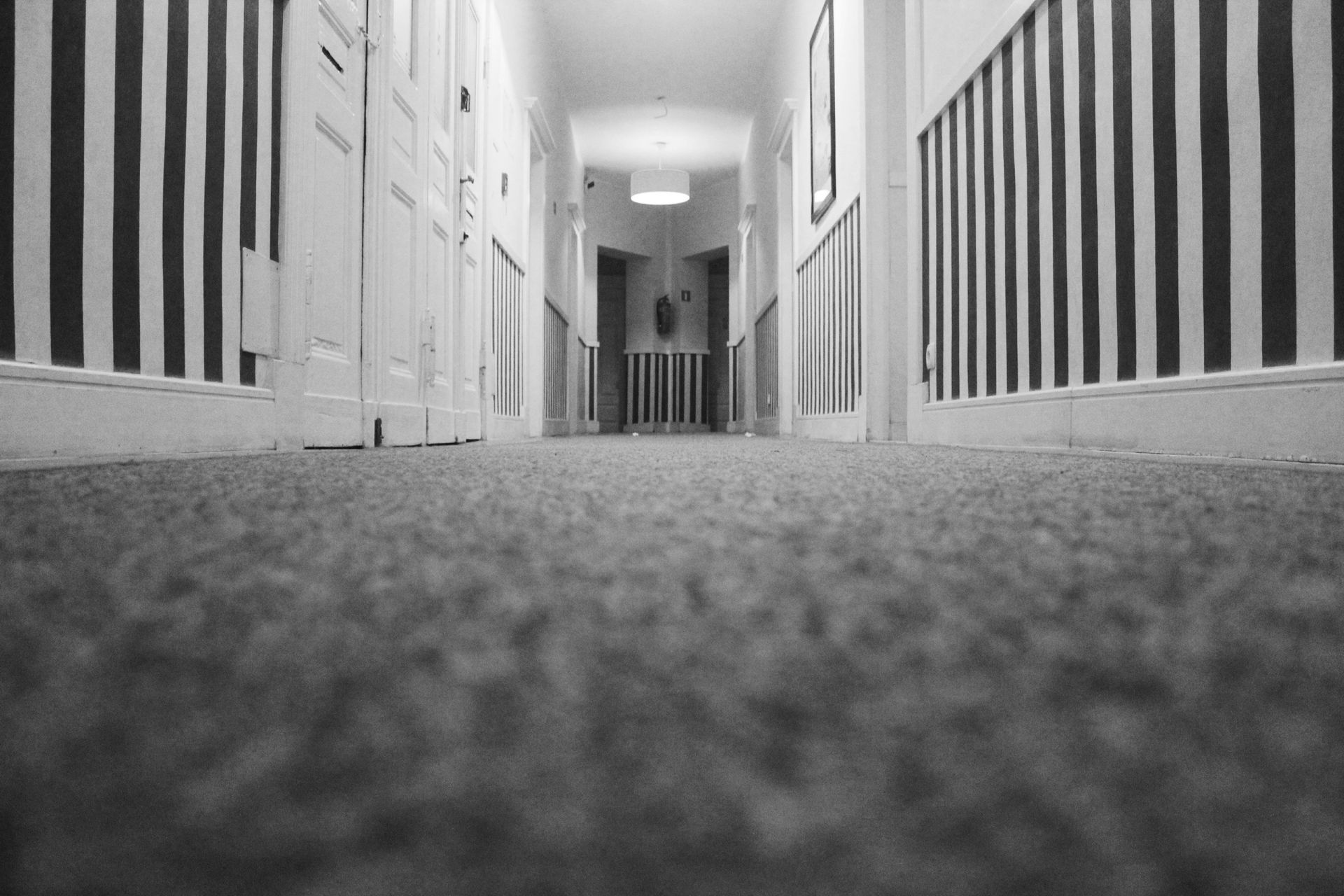 A black and white photo of a hallway with a carpeted floor and striped walls.