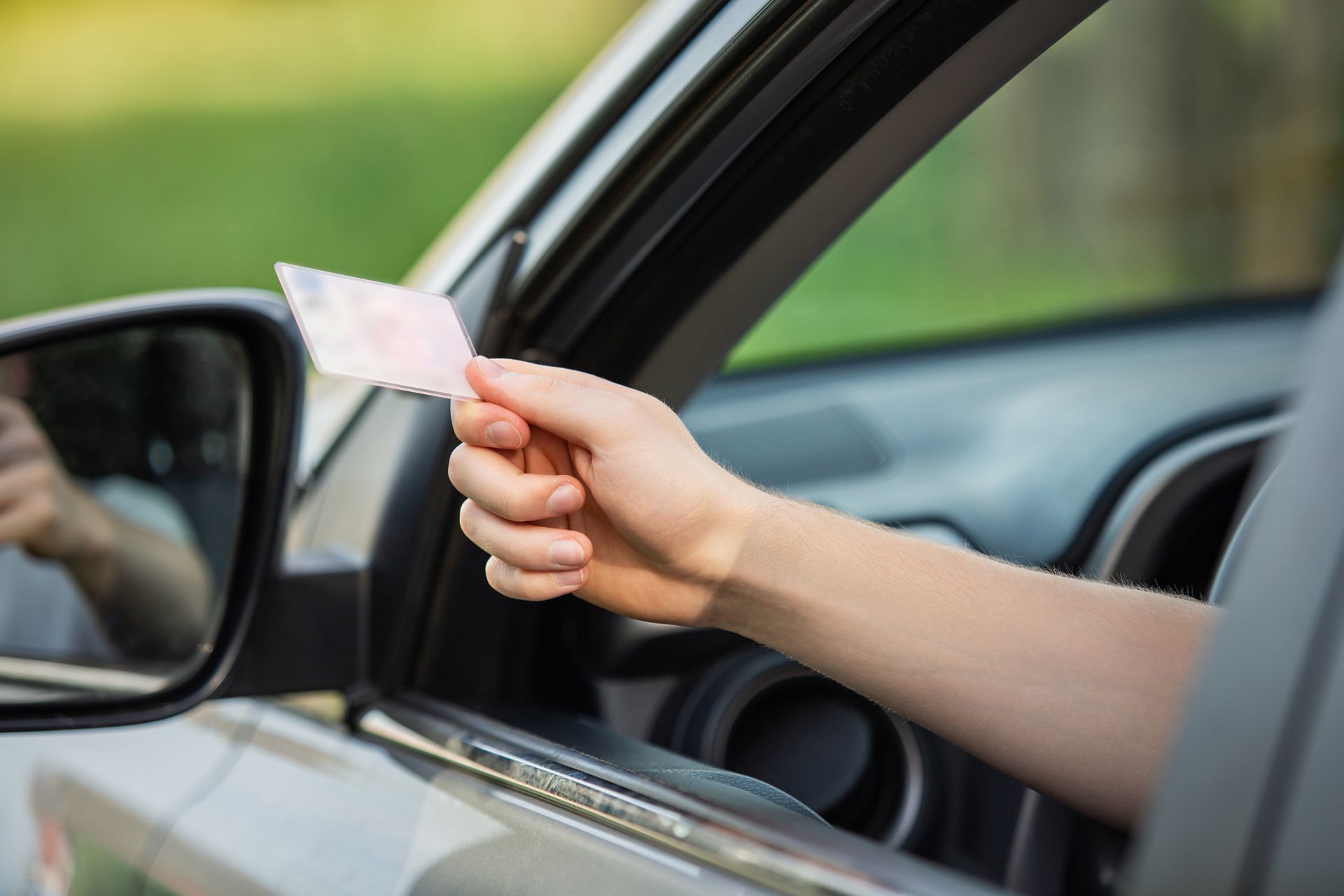 Hand holding driver's license out of a car window, likely for inspection.
