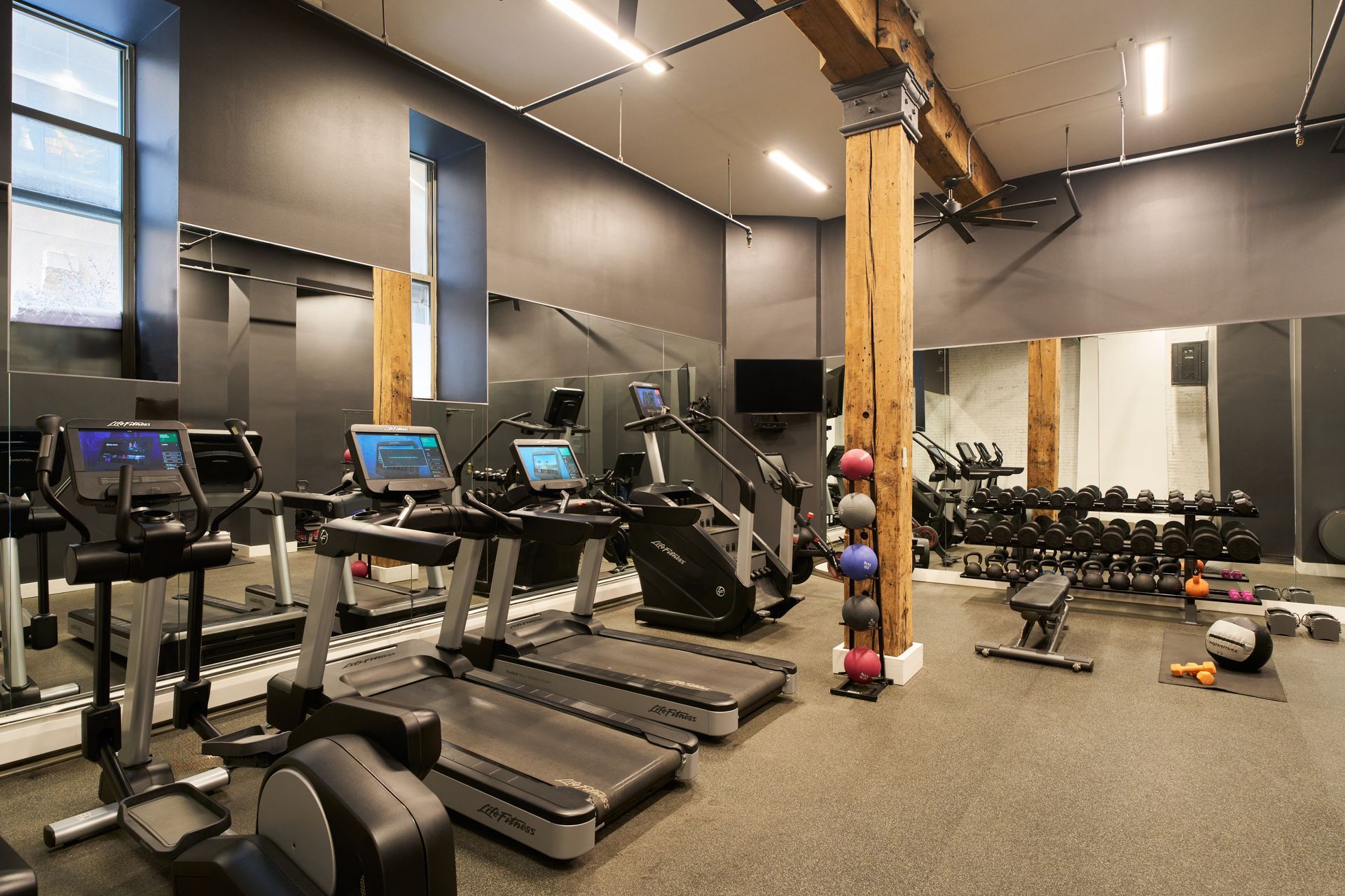 Gym with treadmills, weights, and exercise equipment; gray walls and flooring.