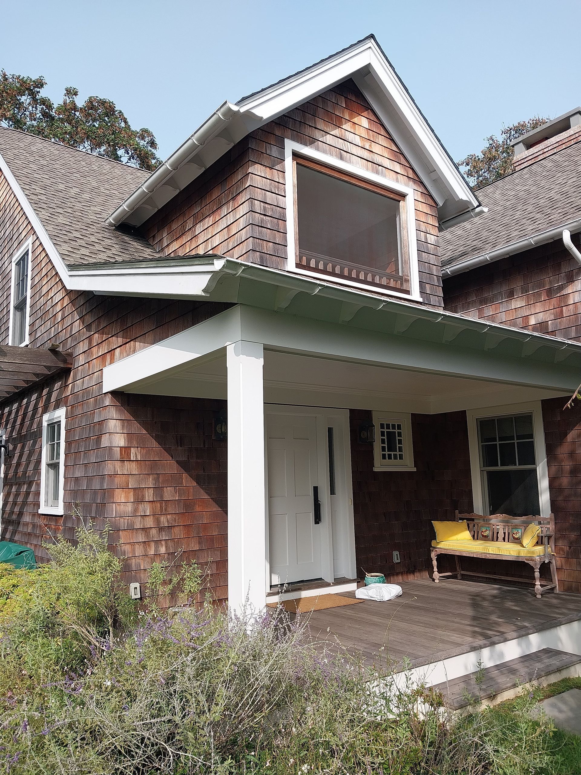 Two-story house with brown shingles, a white porch, and a yellow bench.  The house has white trim and small windows.
