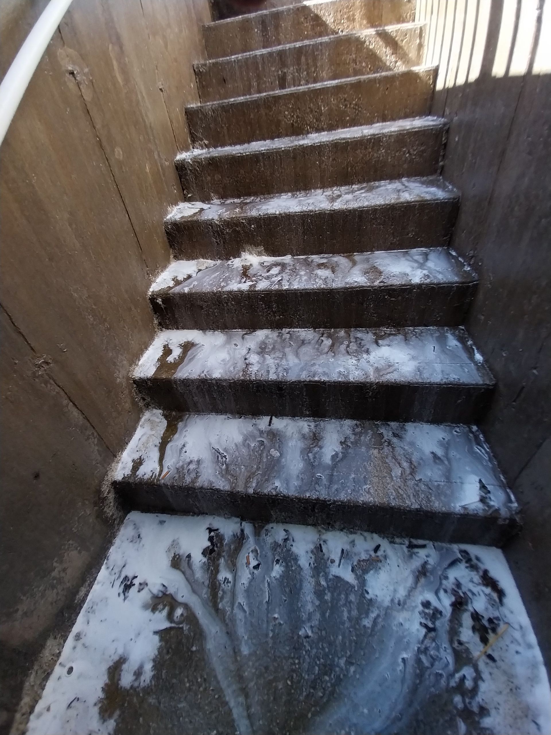 Concrete steps leading upward, covered in a white, foamy substance. The setting appears to be enclosed, possibly a drainage area.
