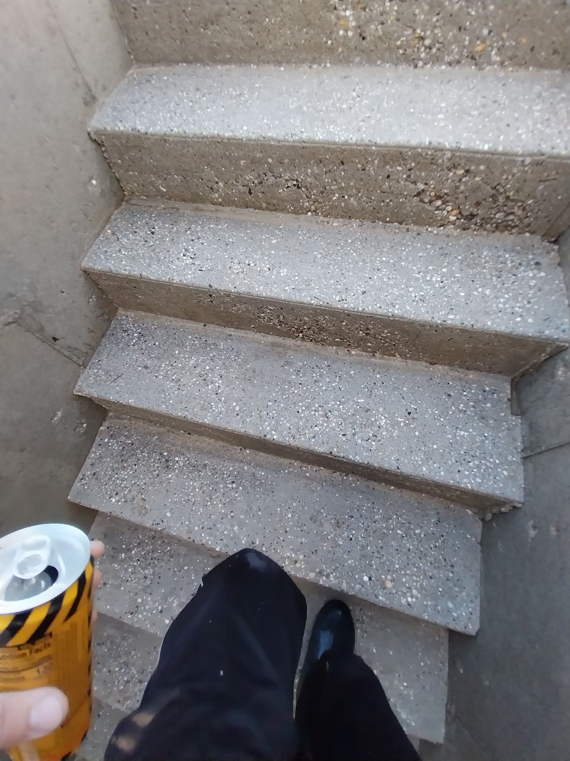 Person descending concrete stairs, holding a can. The stairs are gray and textured.