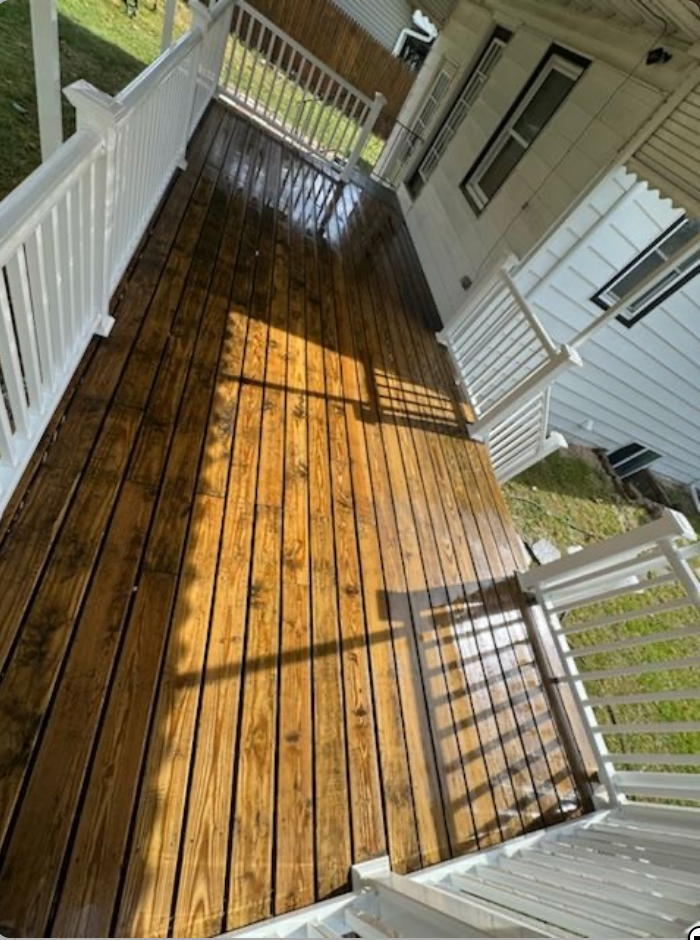 Wooden deck with white railings, recently cleaned and wet. Sunlight casts shadows across the boards.