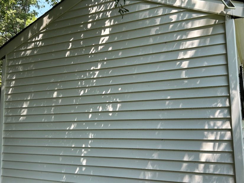 White siding on a building's exterior, with horizontal lines. Shadows from trees cast across the surface.