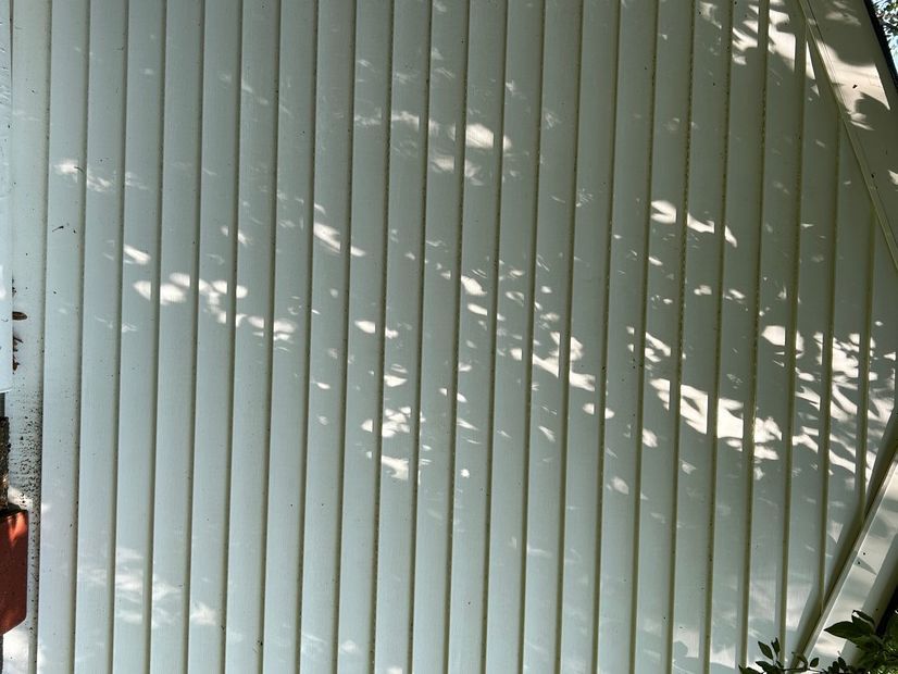 White vertical siding with tree shadows dappling the surface.