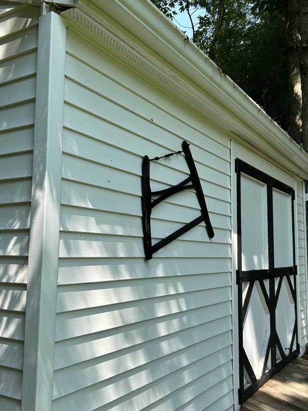 White shed with black trim and a tilted black object mounted on the side. Sunlight casts shadows.