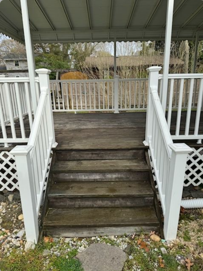 Wooden steps leading up to a deck with white railings and a canopy roof, set in a yard.