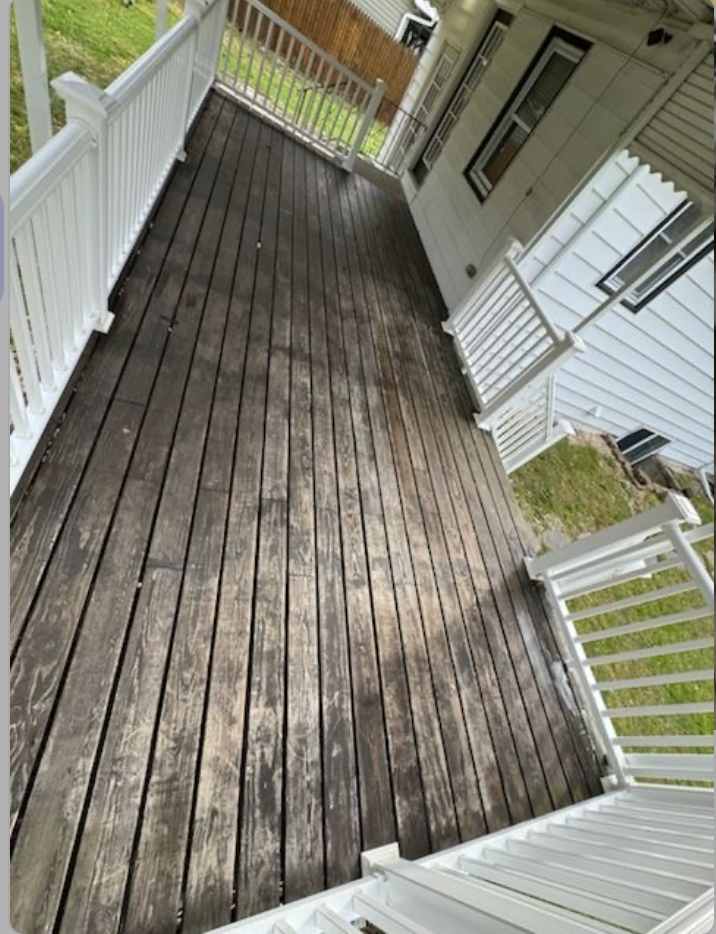 Wooden deck with weathered gray boards, white railing, and a portion of a white house.