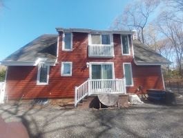 Red house with white trim and a balcony, set against a backdrop of trees and a clear blue sky.