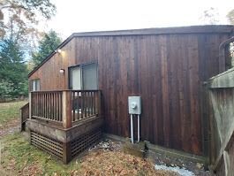 A dark brown wooden house with a small deck, sliding glass door, and an electrical box outside.