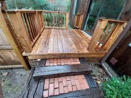 Wooden deck with railing and brick steps leading to a wooden entrance.