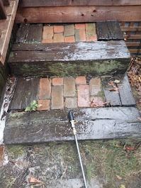 Wooden steps with brick insets, possibly being cleaned with a pressure washer. Steps are outdoors with surrounding grass and leaves.