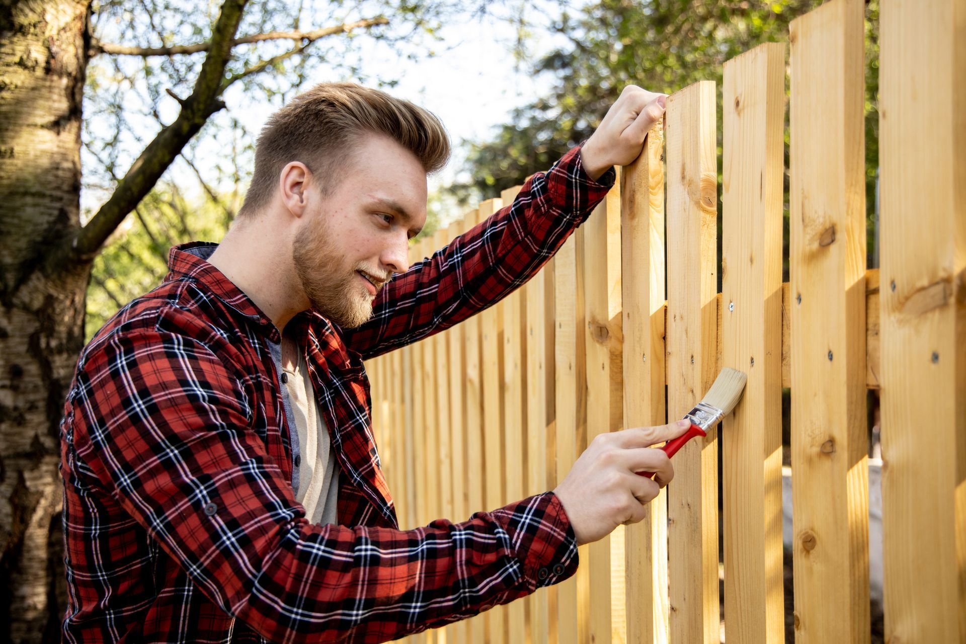 Man painting a fence, showcasing skills of fencing contractors in home improvement projects. Man painting a fence, showcasing skills of fencing contractors in home improvement projects.