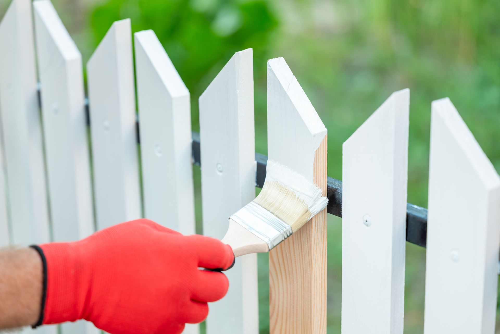 Person paints wooden fence white with handheld brush outdoors.