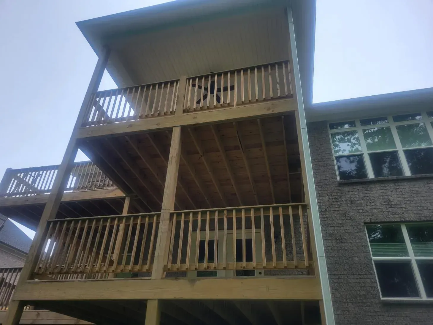 Multi-level wooden deck attached to a brick building, with railings and doors visible.