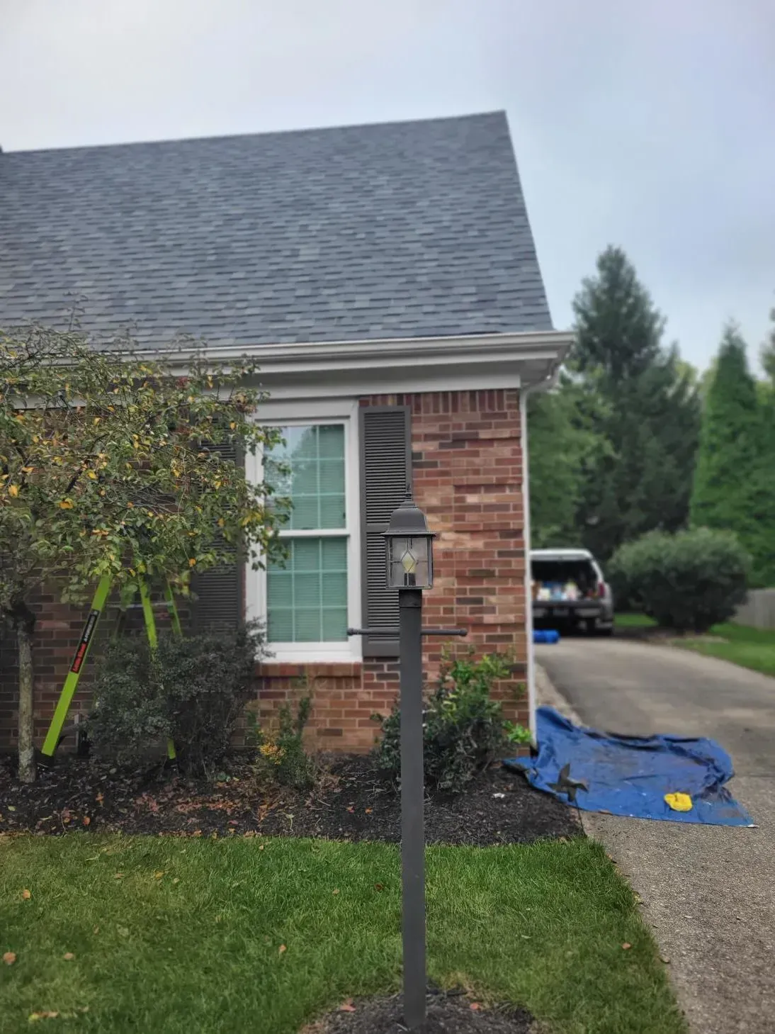 Brick house with window, dark roof, and green lawn; black lamp post in front.