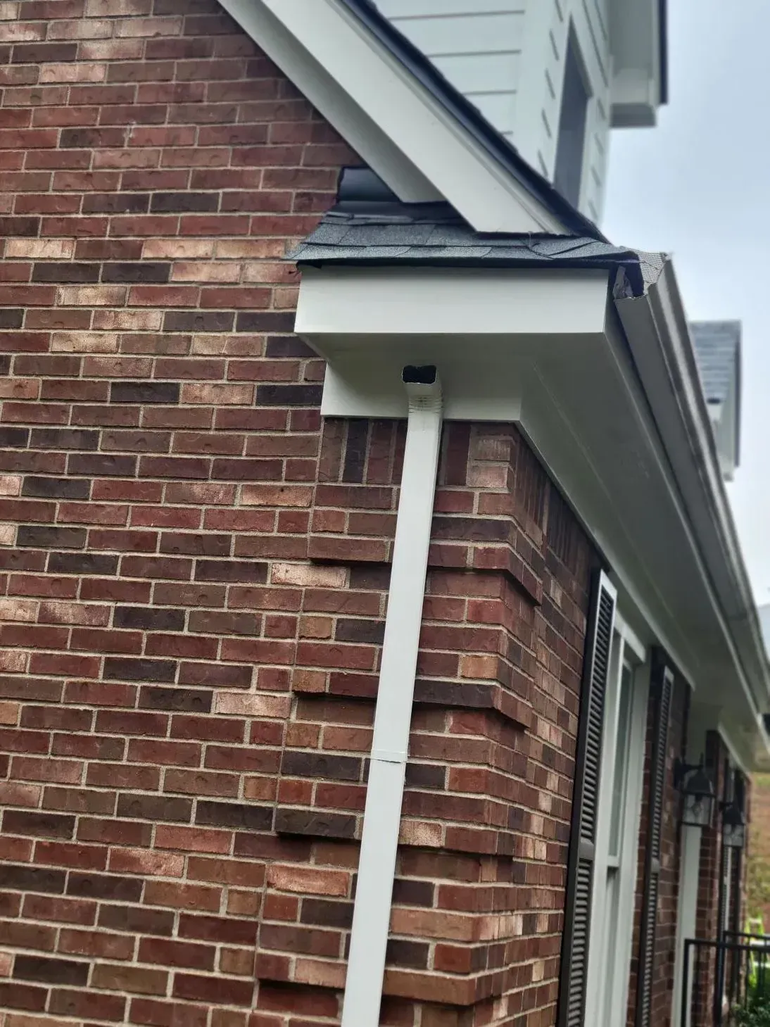 Brick building exterior with white trim, gutters, and a downspout.