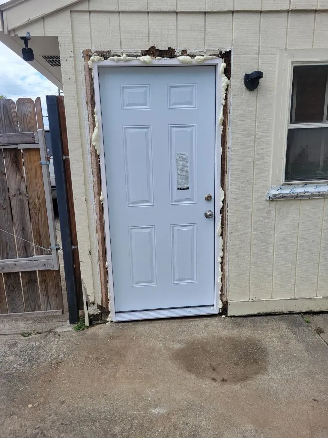White door with window and foam sealant in an exterior wall opening.