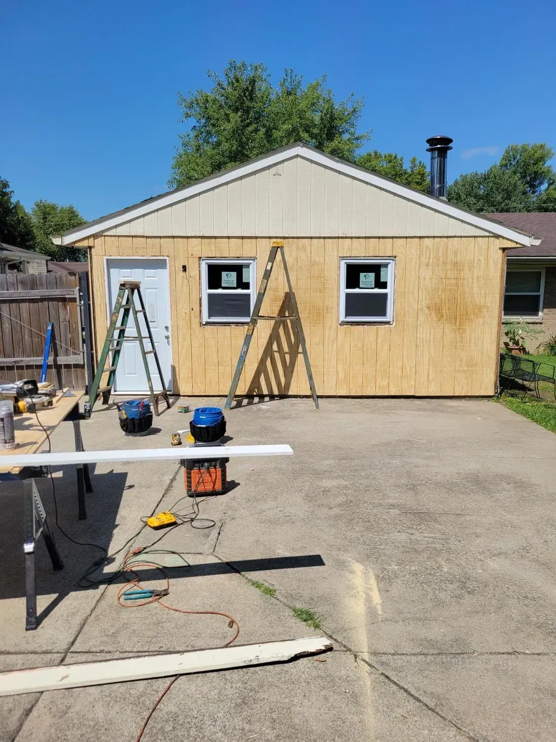 Garage under construction with exposed wood siding and tools scattered on the driveway.