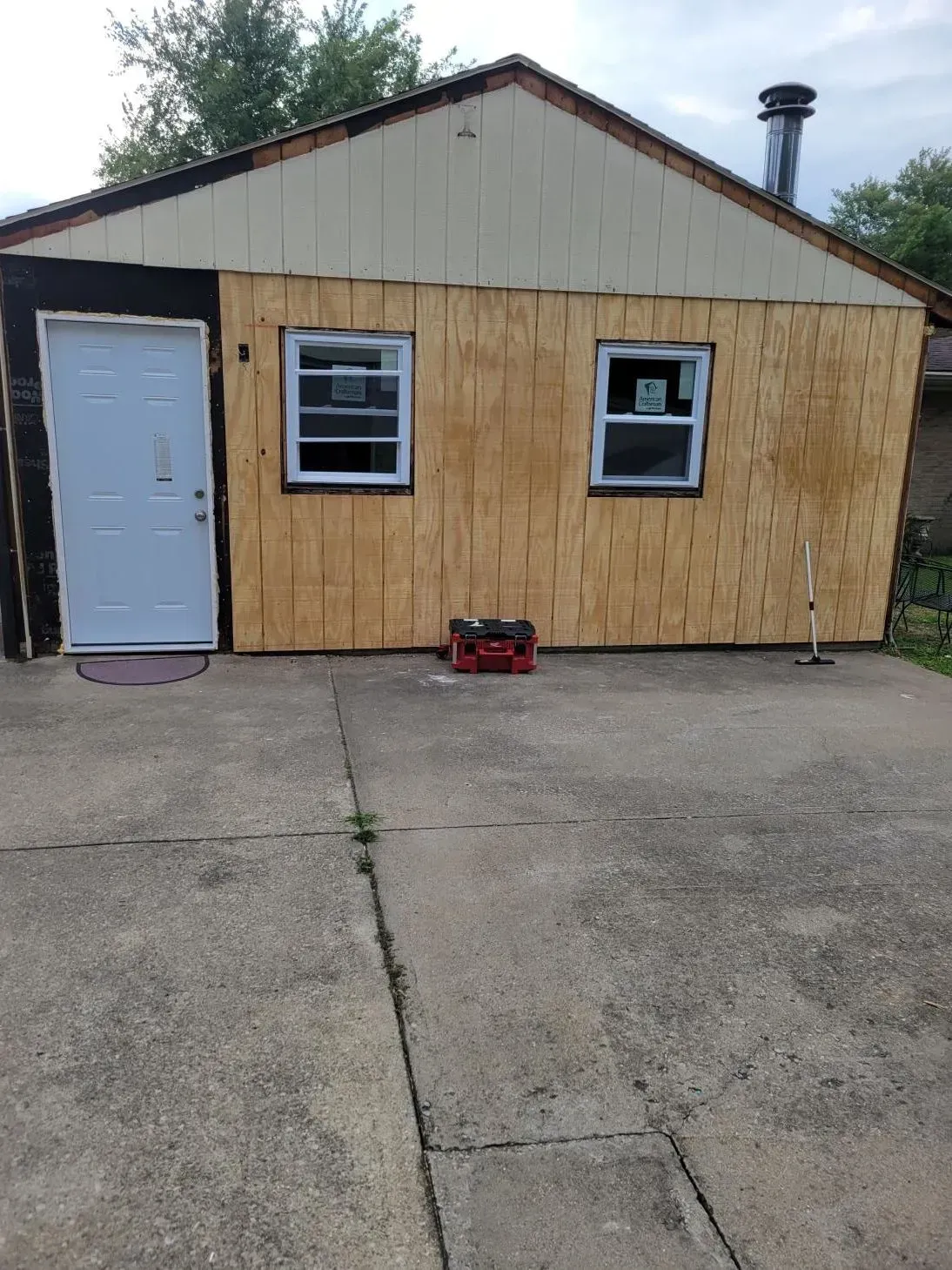 Exterior of a building with unfinished siding, a door, and two windows. Red toolbox and concrete ground.