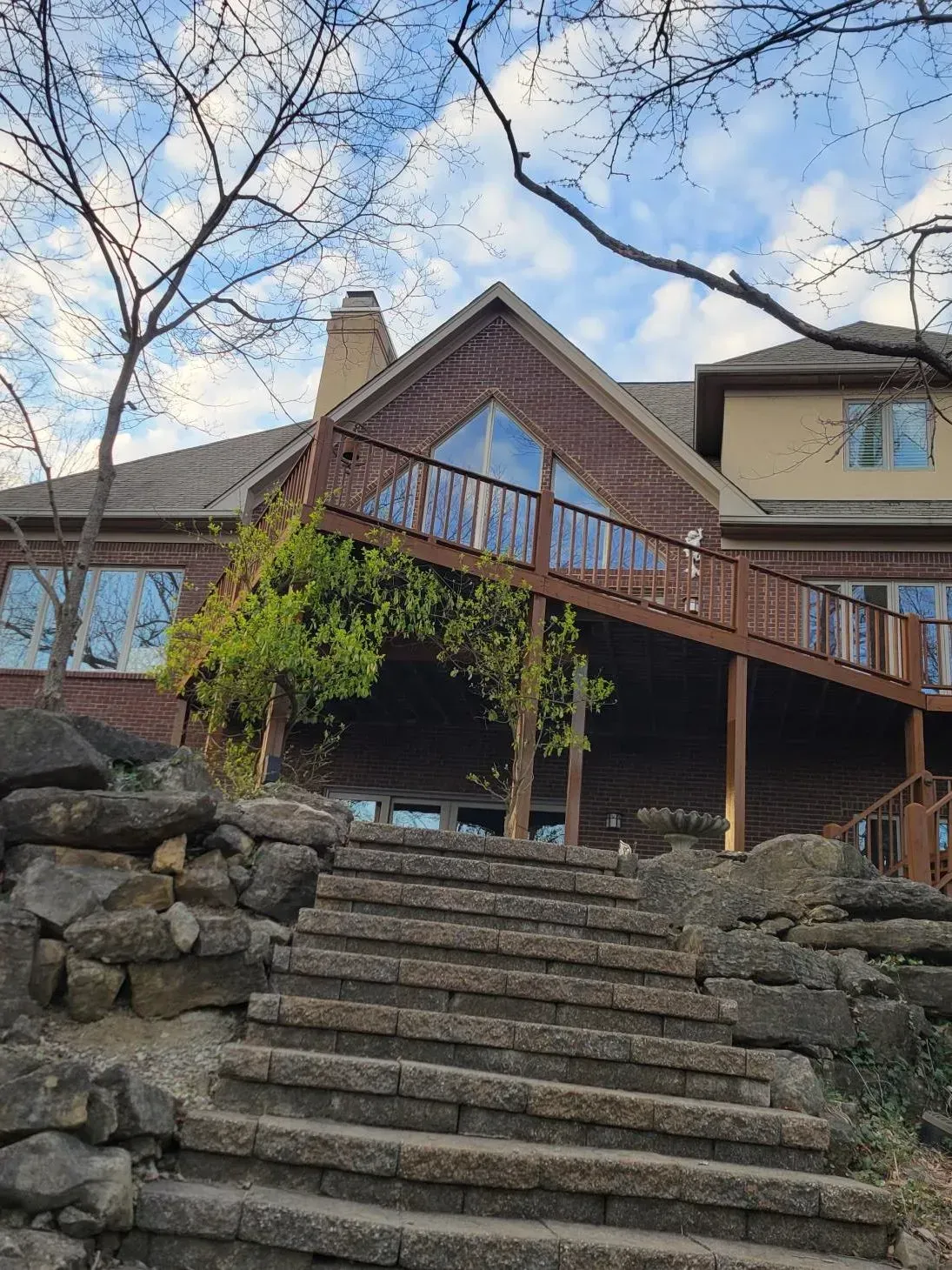 Stone steps leading up to a multi-level home with a wooden deck and brick facade.