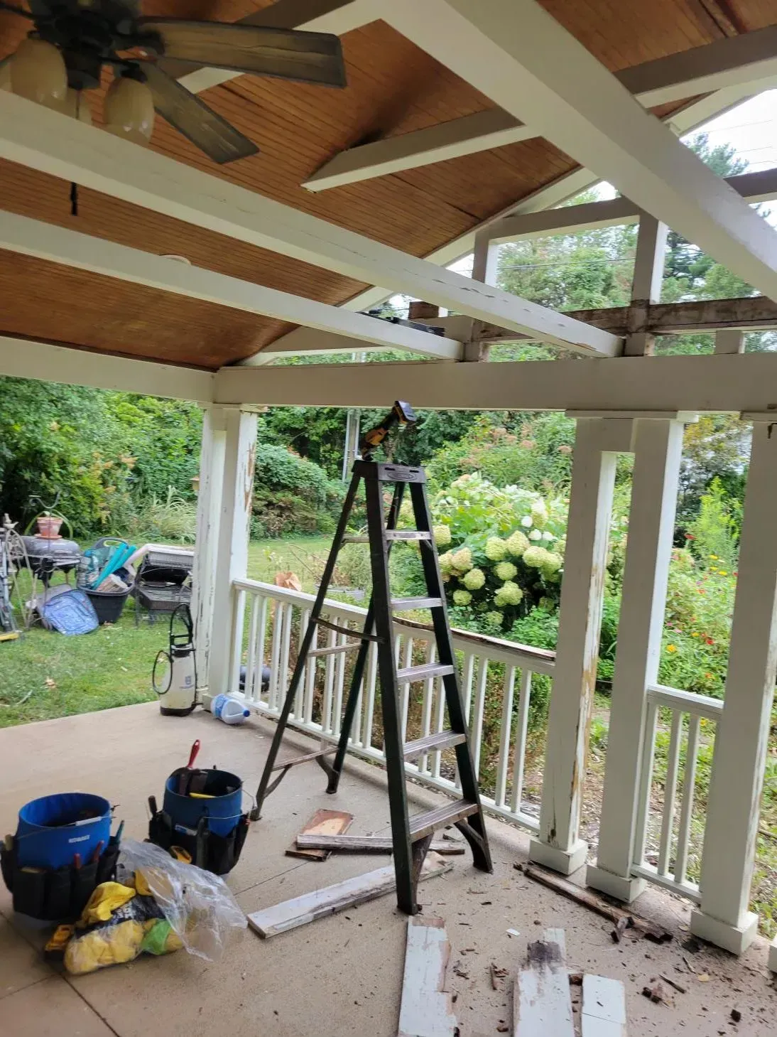 A porch under renovation. A ladder stands between white columns; debris and tools scattered on the ground.