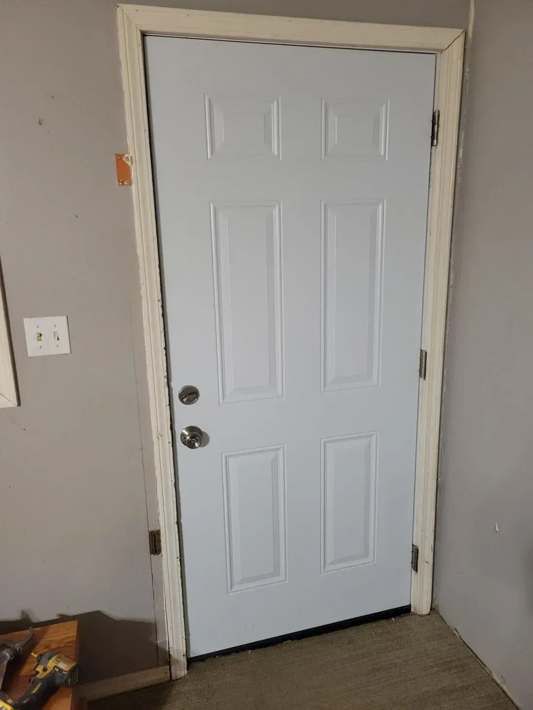 White six-panel door with silver hardware in a room with gray walls, near an electrical outlet.
