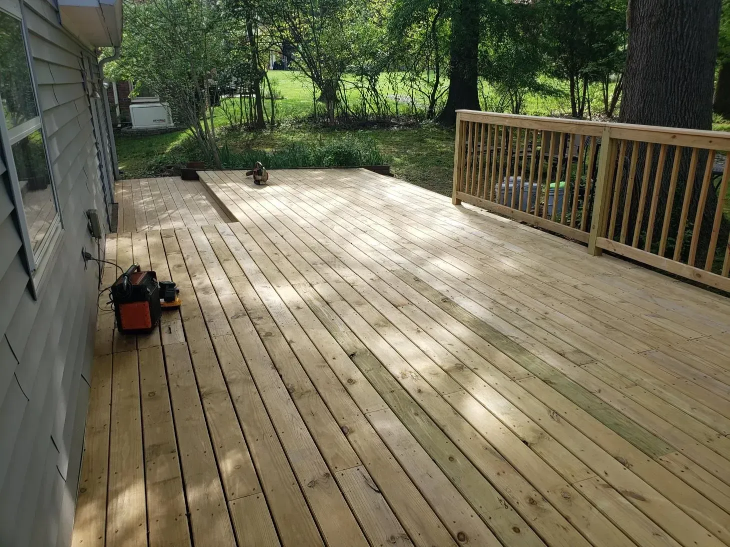 Newly constructed wooden deck with railing next to a house, surrounded by trees and grass.