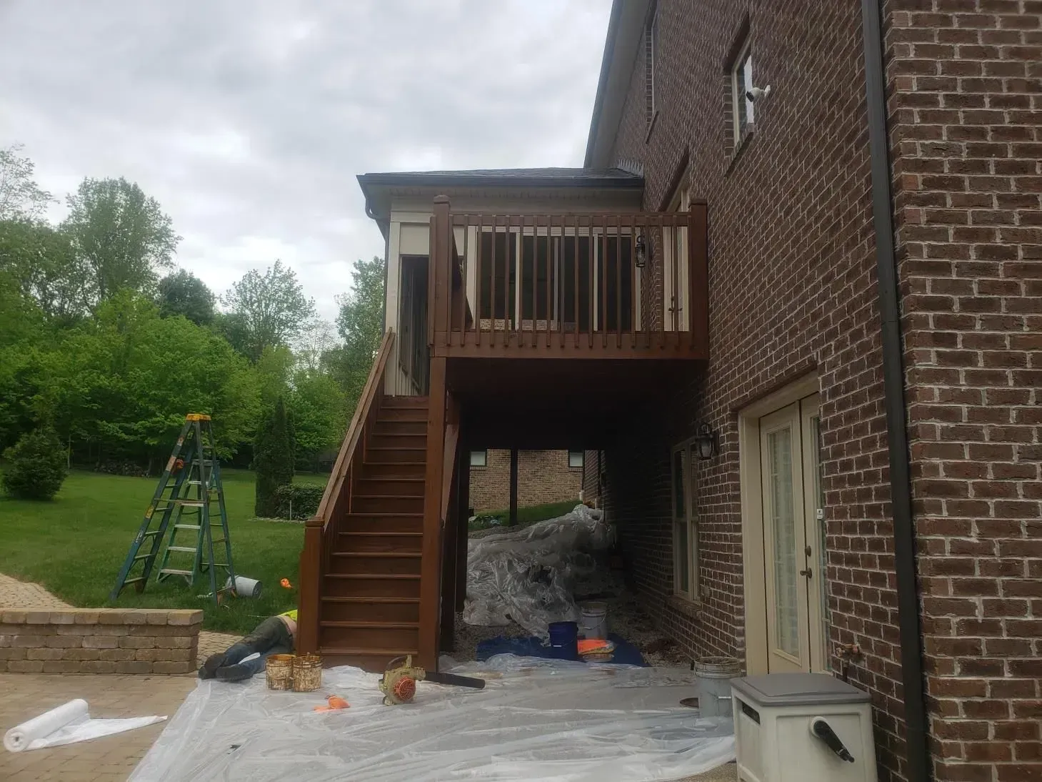 A wooden deck and staircase on a brick house, overlooking a yard; overcast sky.