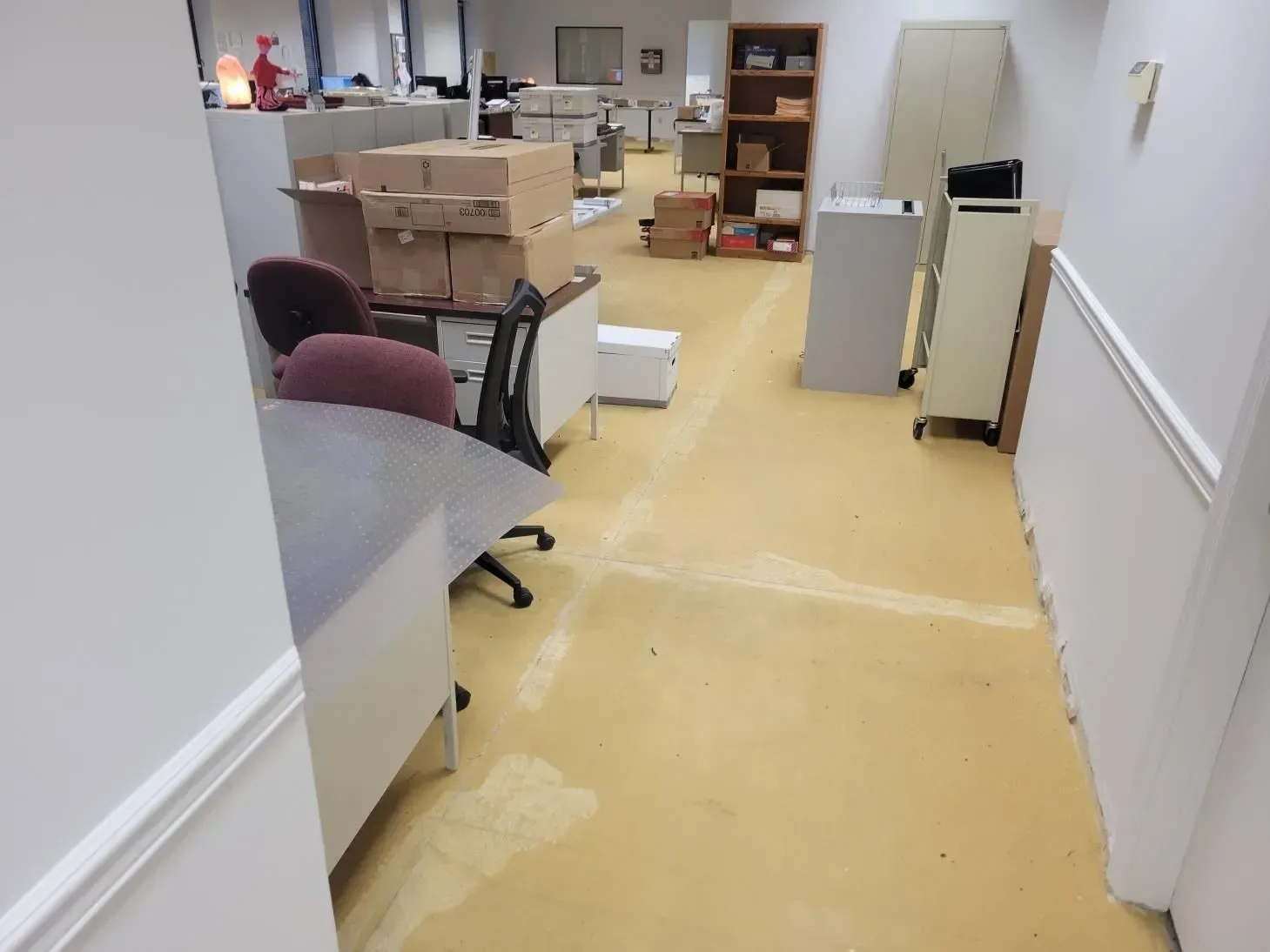 Office with boxes, desks, and a file cabinet; yellow floor, white walls.