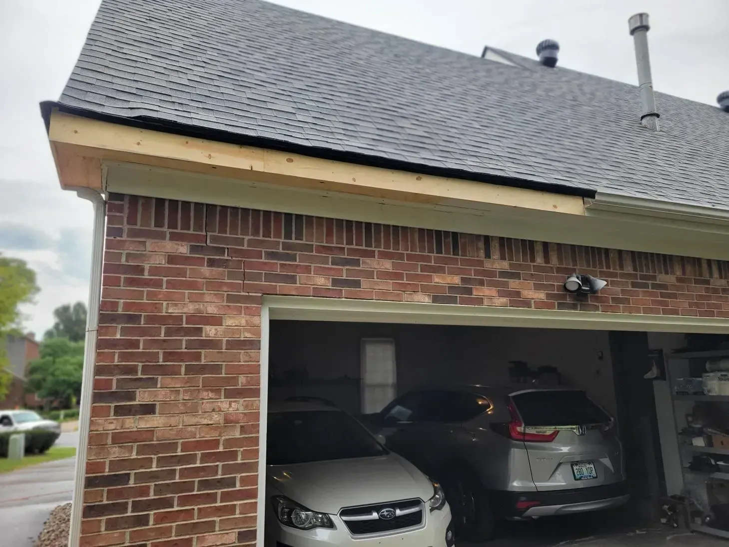 Brick garage with cars inside, a dark roof with new wood trim, and cloudy sky.