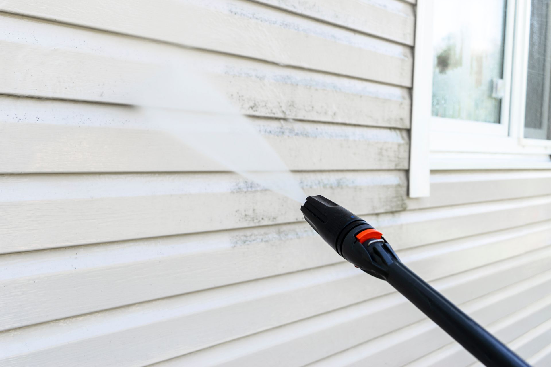 A pressure washer spraying a siding wall to remove dirt and grime.