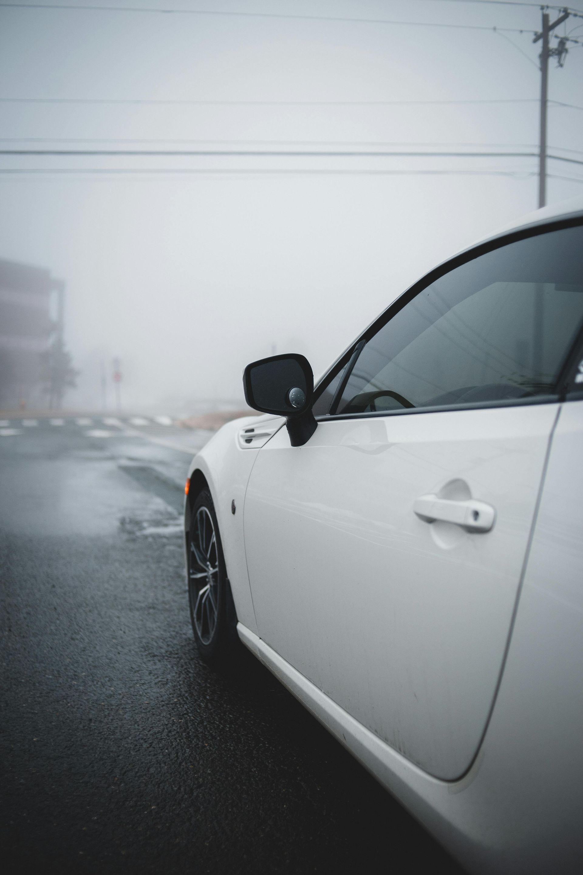 White sports car parked on a wet street with foggy backdrop.