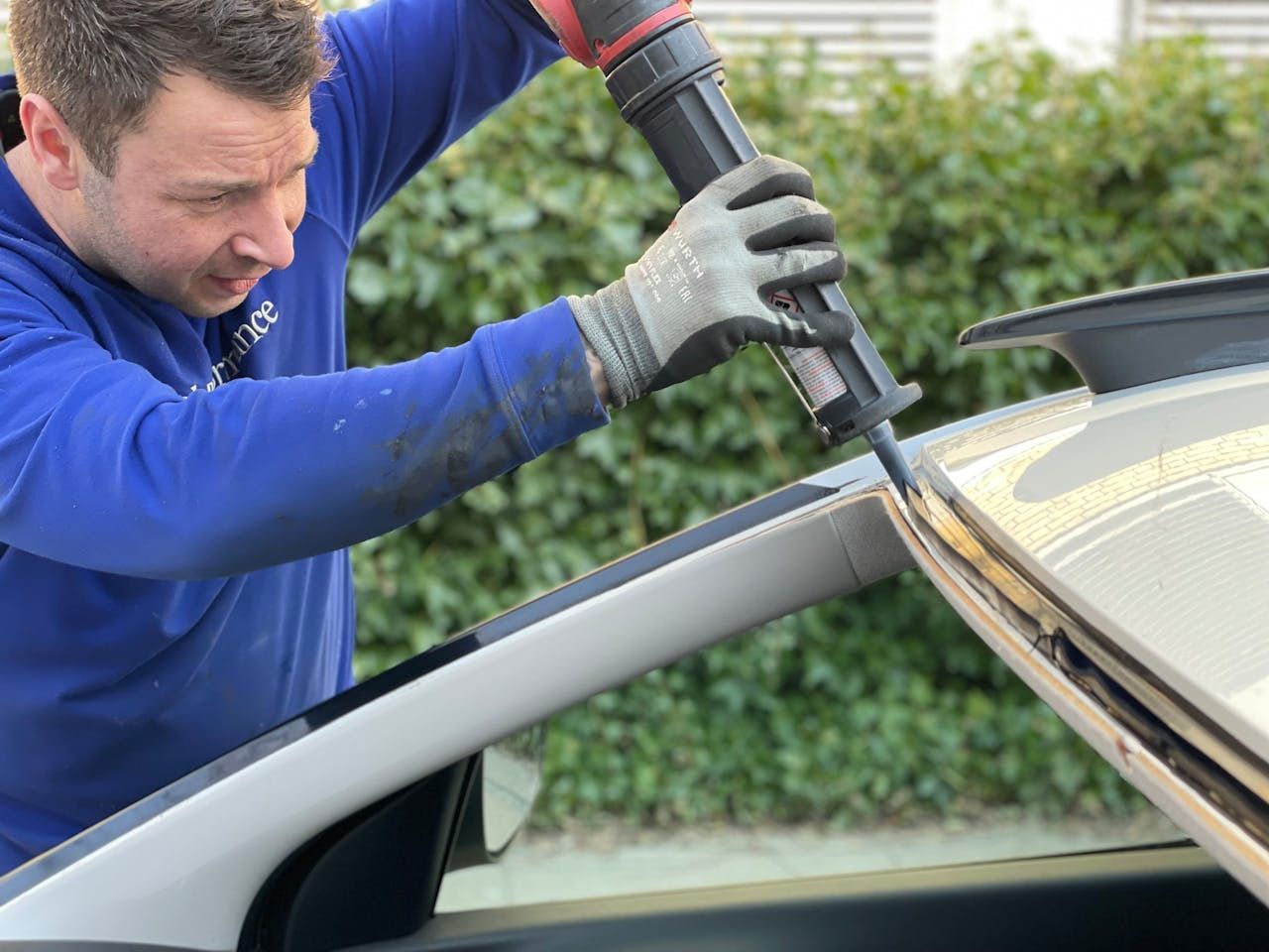 Mechanic cutting a car windshield with a power tool beside a silver vehicle