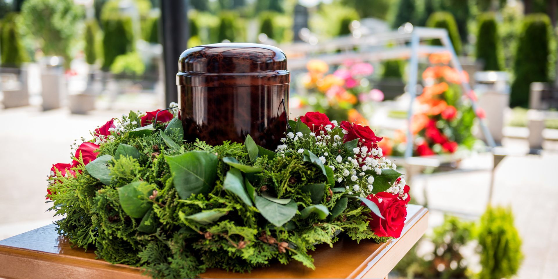 Decorative cremation urn surrounded by red roses and greenery at a cemetery for Cremation Services in Maple Shade, NJ.