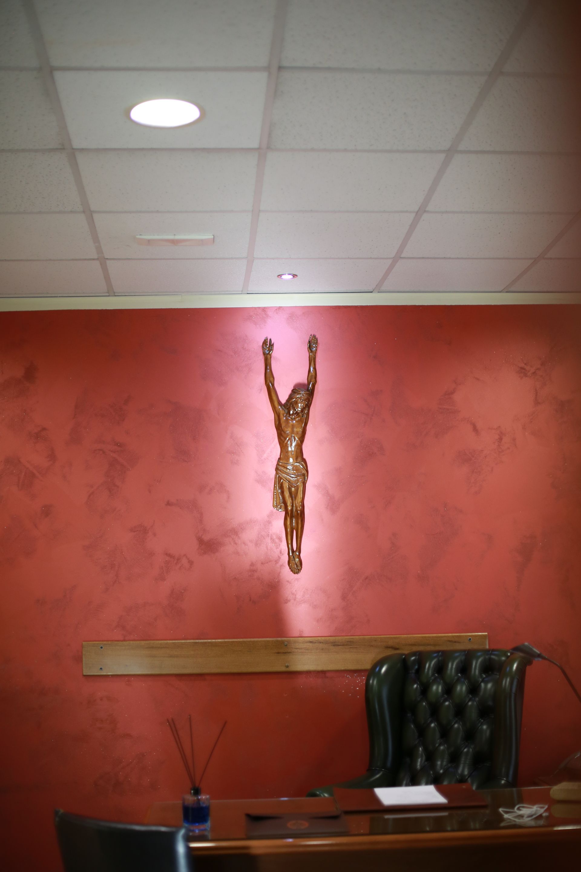 una statua di Gesù è appesa su un muro rosso sopra una scrivania