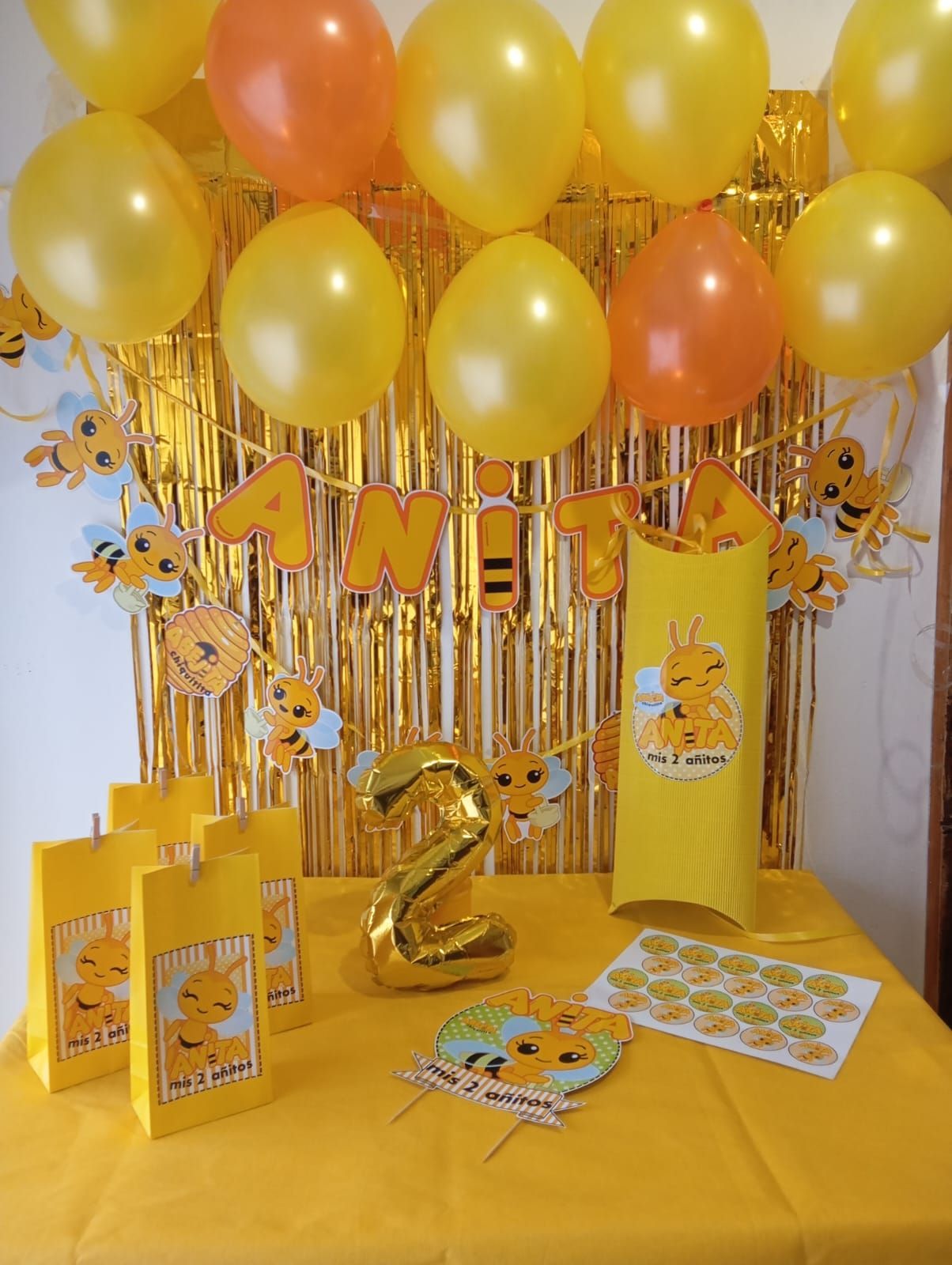 Una fiesta de cumpleaños con temática de abejas amarillas y naranjas, con globos, decoraciones y regalos, para celebrar un segundo cumpleaños.