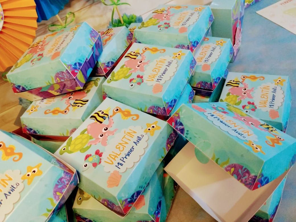 Cajas de regalo con temática marina, apiladas, con dibujos de criaturas marinas y el nombre "Valentín".