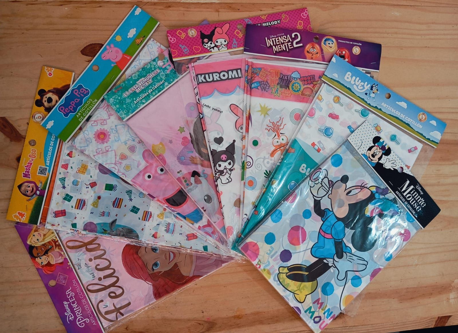 Una colección de coloridas bolsas de regalo de plástico con temática de personajes, incluidos Disney y otros personajes animados, exhibidas sobre una superficie de madera.