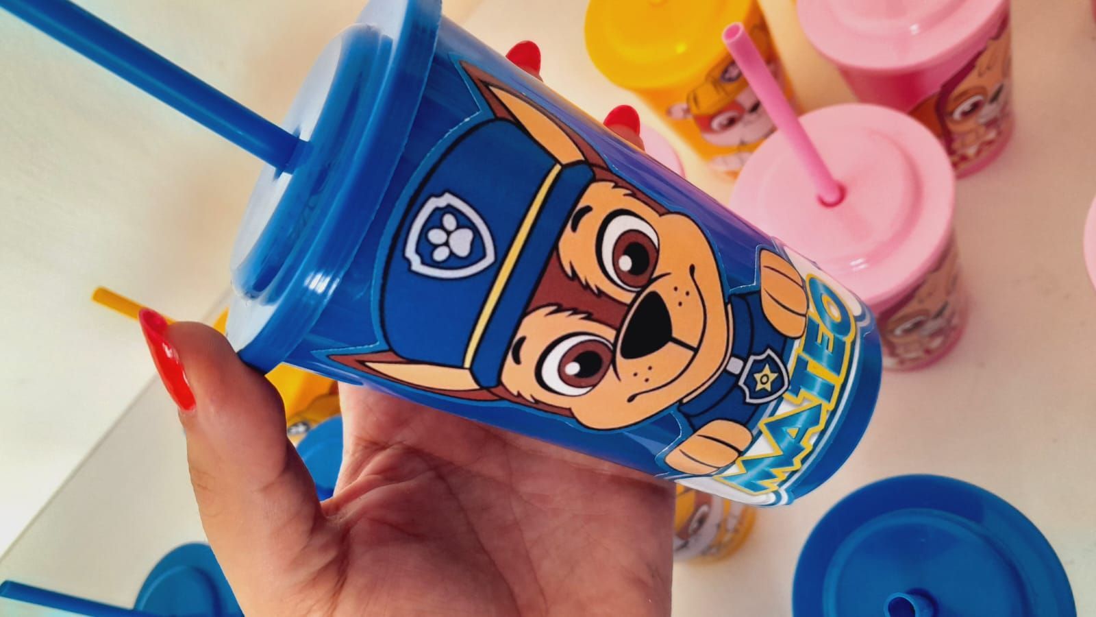 Una persona sostiene un vaso azul de Chase de la Patrulla Canina con una pajita. Al fondo se ven otros vasos de la Patrulla Canina.