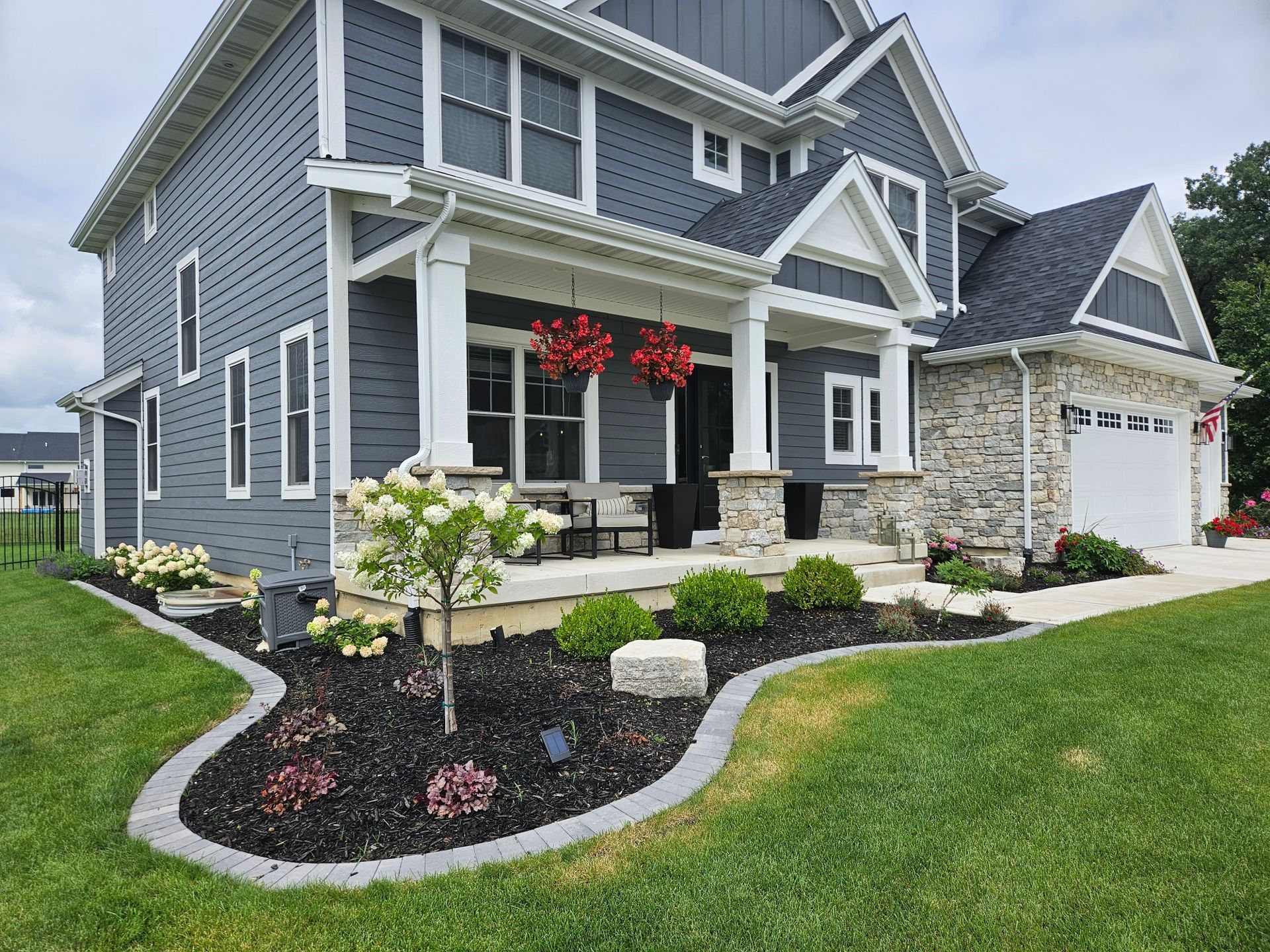 A large gray house with a large porch and a white garage.