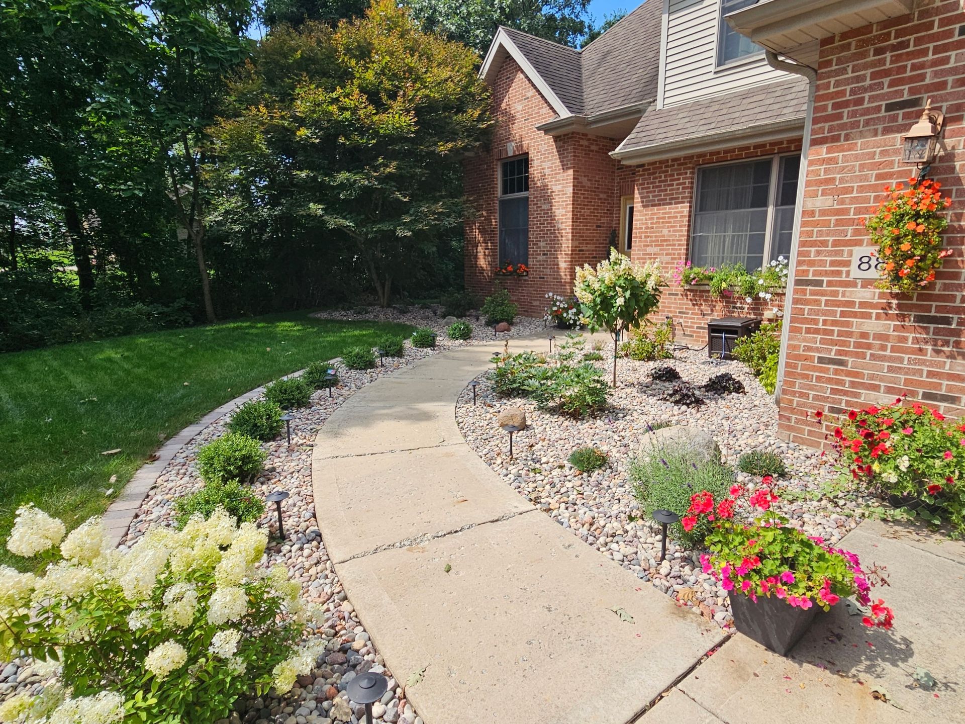 A brick house with a walkway leading to it and flowers in front of it.